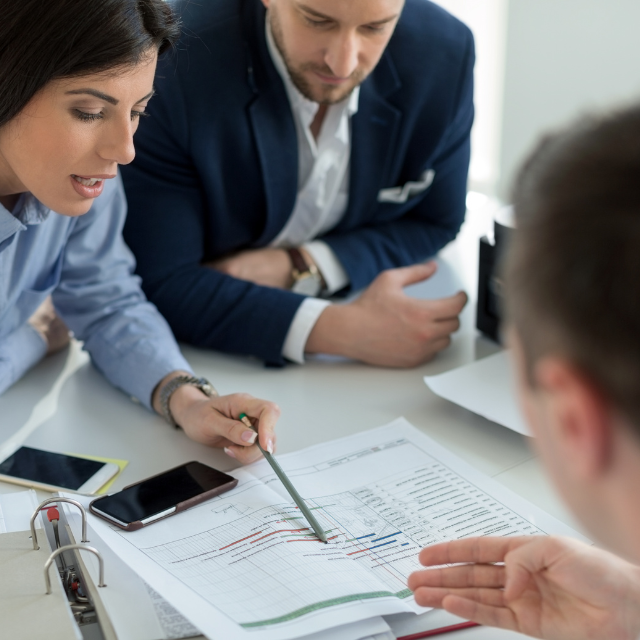 Personnes discutant autour d'une table, examinant des documents avec graphiques, un stylo dans la main et des appareils mobiles présents, représentant l'importance de la collaboration et de la technologie dans le cadre du RGPD.
